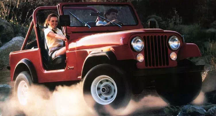 A man and a woman driving a red painted jeep wrangler on a dirt road